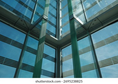 A worm's-eye view looking up at the interior corner of a modern building, showing a complex structure of blue-tinted glass panels and steel support beams. 