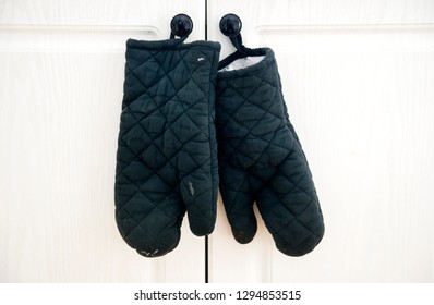 Worn Black Oven Gloves Are Shown Hanging From A Kitchen Cabinet