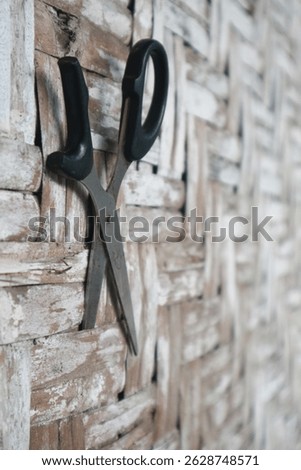 Worn and damaged scissors hang on a textured, rustic wall, showing signs of age and disrepair.

