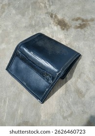 A worn, dark blue leather wallet with visible stitching on a textured gray surface. Open and empty.