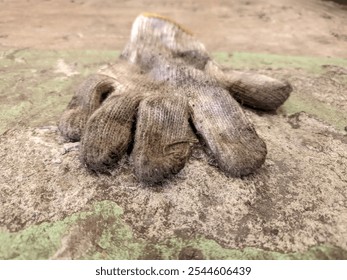 A worn, dirty glove on a rough surface, symbolizing industrial safety and personal protective equipment (PPE) in challenging work environments - Powered by Shutterstock