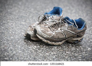 Worn, Dirty, Smelly And Old Running Shoes On A Tarmac Road. Road Running, Endurance, Marathon Aftermath And Active Lifestyle Concept. 