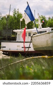 Worn French Flag On Boats On Dry Land During Low Tide In Small Port In Gironde, France
