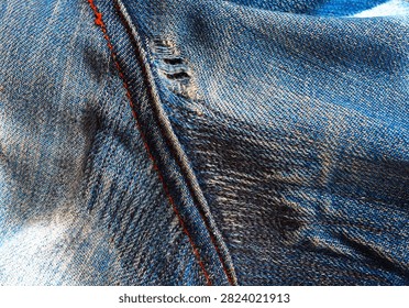 Worn jeans after darning. The darned jeans have become worn and have become frayed and torn again. Close view of denim fabric showing stitching and wear patterns on jeans. Close-up look at blue denim with visible stitching and signs of wear. The fabric appears textured with areas of fading. Hole in pants, darning, sewing, clothing repair.