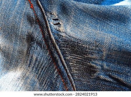 Worn jeans after darning. The darned jeans have become worn and have become frayed and torn again. Close view of denim fabric showing stitching and wear patterns on jeans. Close-up look at blue denim with visible stitching and signs of wear. The fabric appears textured with areas of fading. Hole in pants, darning, sewing, clothing repair.