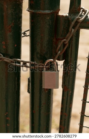 Worn lock and chain on aged green gate indicating protection. Weathered and rusted lock and chain attached to old green gate demonstrating security measures