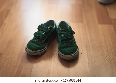 Worn And Muddy Pair Of Childs Shoes On A Wooden Floor Of A Living Room.