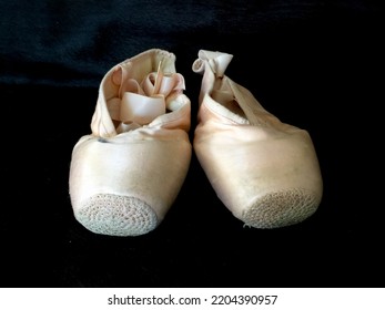 A Worn Pair Of Ballet Pointe Shoes On A Black Background