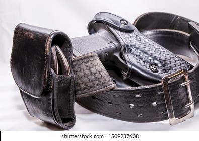 A Worn Police Duty Belt With A Black Pistol And Handcuff Case Wrapped Up On A White Background