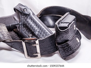 A Worn Police Duty Belt With A Black Pistol And Two Pistol Magazine Case Wrapped Up On A White Background