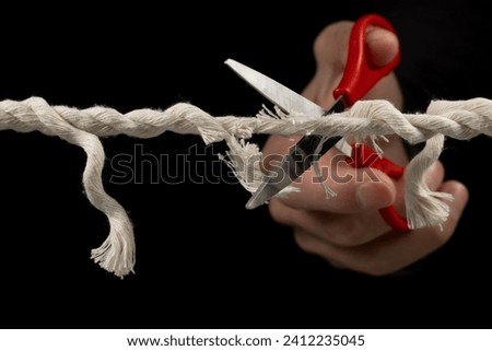 Worn rope ready to break, with scissors on black background