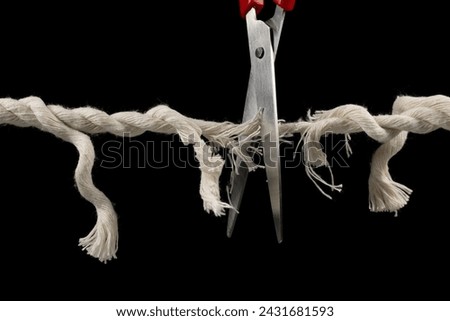 Worn rope ready to break, with scissors on black background