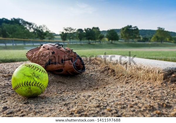 Worn softball and glove on pitcher\'s mound in\
early morning
