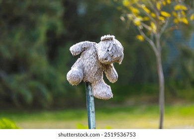 A worn, stuffed toy dog is impaled on a metal pole, set against a soft-focus, natural outdoor background. - Powered by Shutterstock