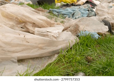 Worn translucent plastic sheets and dirty fabric pieces strewn across a patch of green grass, creating a messy outdoor scene. The foreground shows crumpled