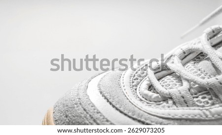 A worn white sneaker featuring mesh and suede texture with a yellowed sole and detailed stitching, laces neatly tied.