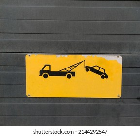 Worn Yellow Tow Truck Traffic Warning Sign, Vehicles Will Be Towed, On Dark Wood Panel Background Wall. With Space For Copy Text On Sign Under Truck And Car.