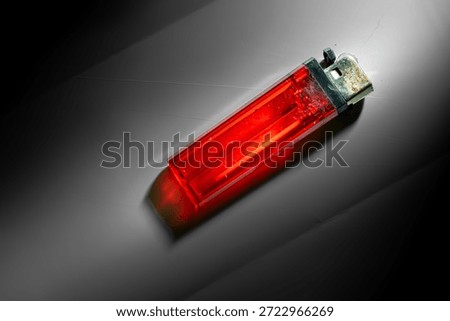Worn-out red plastic lighter with dramatic lighting on a minimalist dark background