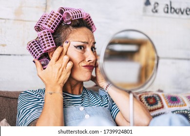 Worried Adult Young Caucasian Female Check Wrinkles And Aging Time Effect On Her Face Skin - Beautiful Funny Woman With Make Up And Curlers On Hair At Home In Getting Ready Activity