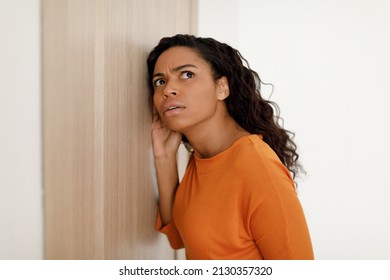 Worried African American Woman Listening Through Closed Door To Secret Information And Gossips, Eavesdropping Holding Hand Near Ear Standing At Home. Concerning News, Overhearing Concept - Powered by Shutterstock