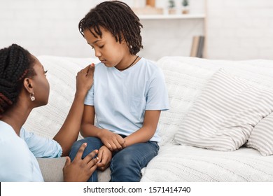 Worried African Mother Saying Sorry To Her Sad Child Sitting On The Couch At Home. Free Space