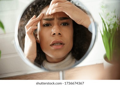 Worried African Teen Girl Checking Facial Skin Problem Look In Mirror. Young Woman Touch Face Squish Pop Zit Pimple On Forehead Depressed By Blackheads. Black Skin Care Problem Self Care Concept.