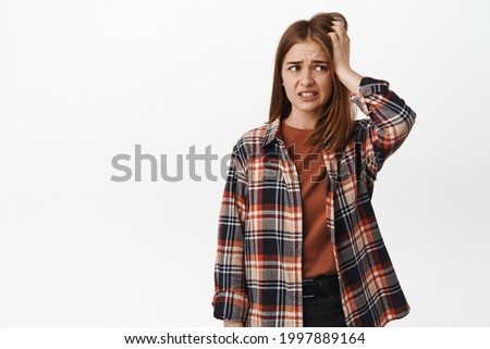 Worried and anxious blond girl scratch head, looking aside and panicking, feel nervous or indecisive, dont know what to do, standing against white background