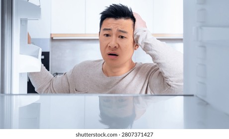 Worried Asian Man Checking Empty Fridge At Home, Kitchen Situation, Food Wastage Concept