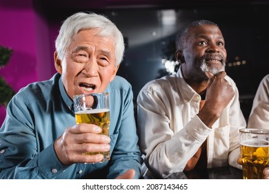 Worried Asian Man Holding Glass Of Beer While Watching Football With Interracial Friends In Pub