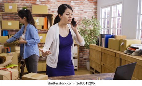 Worried Asian Pregnant Woman Talking On Smartphone Tense Angry Mad. Nervous Young Motherhood Lady Start Up Business Deal With Problem Argue On Mobile Phone Online Shop Office. Girl Colleague Packing