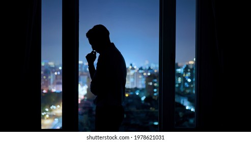 worried asian young businessman is standing near windows while working overtime in office at night - Shutterstock ID 1978621031