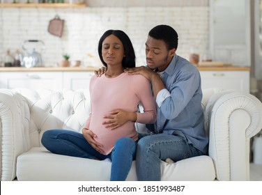 Worried black husband supporting pregnant wife with prenatal contractions at home. Beautiful African American woman suffering from pain, giving birth to baby with help of her partner