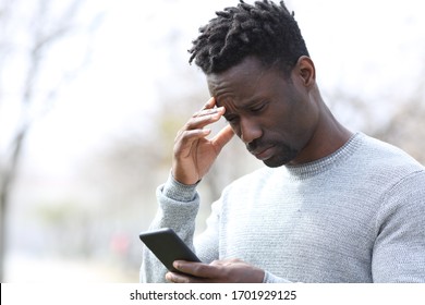 Worried Black Man Reading Bad News On Smart Phone Standing At Park