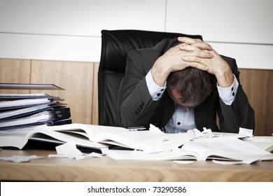Worried businessman in dark suit sitting at office desk full with books and papers being overloaded with work. - Powered by Shutterstock