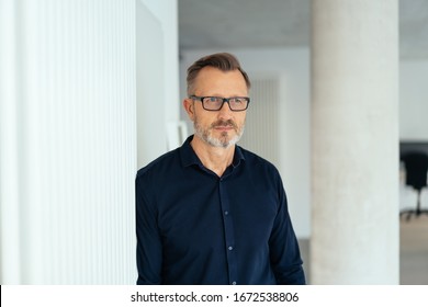 Worried Businessman Staring Intently Ahead With A Grim Expression As He Stands Against A Wall In The Office With Copy Space