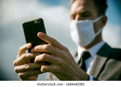 Worried businessman wearing surgical face mask checking his smartphone for coronavirus news updates outdoors - Shutterstock ID 1684640383