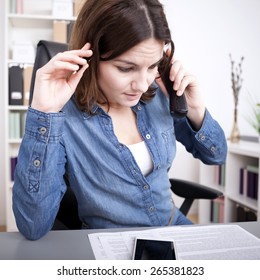 Worried businesswoman taking a phone call frowning as she listens to the conversation while looking at a report spread out on her desk