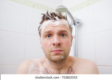 Worried caucasian foamed young man after the water in the shower was turned off, looking at the camera. Shower breakdown or hot water shut-off.