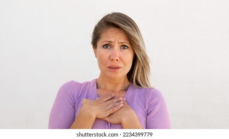 Worried Caucasian woman pressing hands to chest. Portrait of sympathetic mature female model with fair hair in lilac blouse looking at camera, reacting to something sad. Anxiety, sympathy concept - Powered by Shutterstock