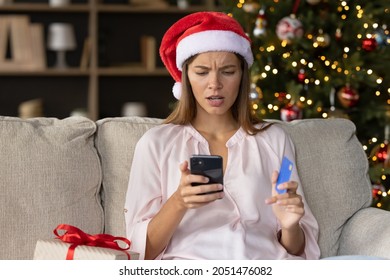 Worried Concerned Girl In Christmas Santa Hat Having Problems With Payment By Credit Card Online For New Year Purchases, Looking At Smartphone Screen With Puzzled Face. Scam, Fraud Concept