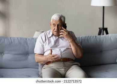 Worried concerned senior elder man talking on cellphone to doctor, feeling unwell, calling for emergency, ambulance, sitting on sofa at home, contact helpline, using mobile phone - Powered by Shutterstock