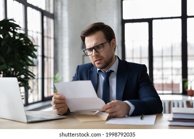 Worried confused businessman reading letter at workplace, holding paper document. Business leader receiving bankruptcy or eviction notice, loan rejection from bank, getting bad news from mail