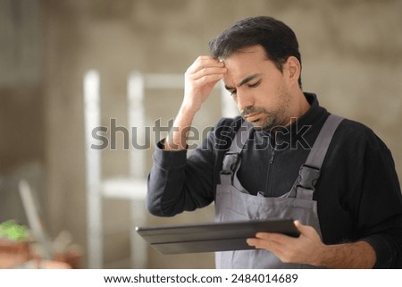Worried construction worker checking tablet in a house