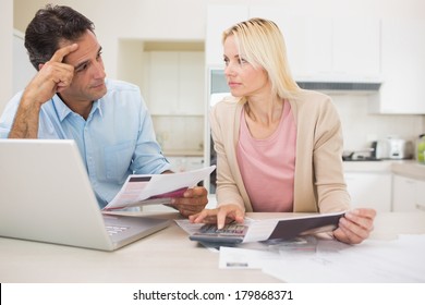 Worried Couple With Bills And Laptop In The Kitchen At Home