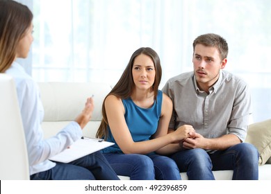 Worried couple listening to marriage counselor during a therapy sitting on a sofa at home