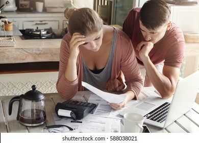 Worried Couple Reviewing Their Family Finances And Calculating Expenses, Trying To Save Some Money To Pay Off Loan In Bank, Reviewing Bills Together, Using Laptop And Calculator At Kitchen Table