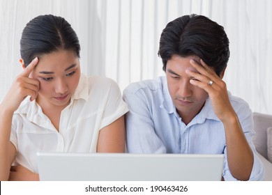 Worried Couple Using Laptop Together At Home In The Living Room