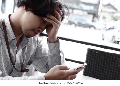 Worried depressed young Asian businessman looking mobile smart phone. Anxiety business concept.