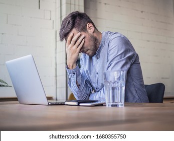 worried and disappointed remote online working man in casual outfit with laptop sitting in an coworking home office at a work desk