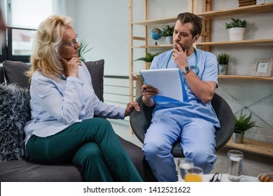 Worried Doctor Thinking While Analyzing Medical Reports Of Mature Woman During Home Visit. 